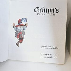Puede incluir: Libro abierto con el t&iacute;tulo "Grimm's Fairy Tales" en negro. Ilustraci&oacute;n de un gnomo con sombrero y botas rojas. Texto: "Abridged by SHIRLEY DEAN" e "Illustrations by HILDA OFFEN".