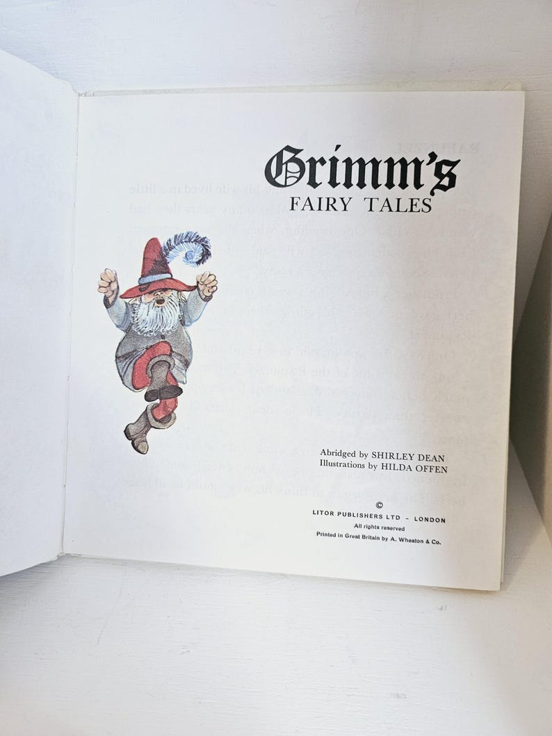 Puede incluir: Libro abierto con el t&iacute;tulo "Grimm's Fairy Tales" en negro. Ilustraci&oacute;n de un gnomo con sombrero y botas rojas. Texto: "Abridged by SHIRLEY DEAN" e "Illustrations by HILDA OFFEN".