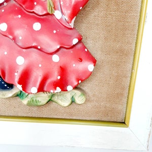 May include: A framed 3D wall art piece featuring a woman in a red and white polka dot dress. The woman is holding a blue and white umbrella. The background is a brown burlap fabric.