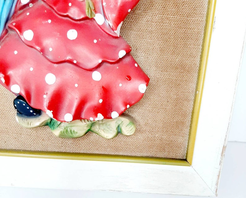 May include: A framed 3D wall art piece featuring a woman in a red and white polka dot dress. The woman is holding a blue and white umbrella. The background is a brown burlap fabric.