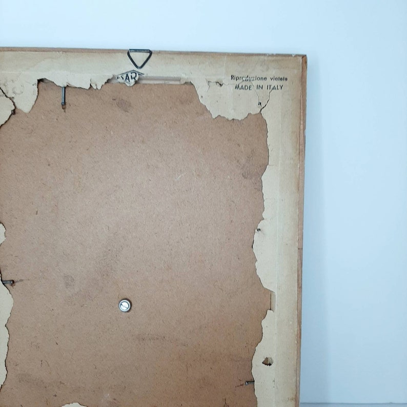 May include: The back of a wooden picture frame with a label that reads "Riproduzione vietata MADE IN ITALY".