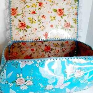 Pu&ograve; includere: Una scatola di immagazzinaggio floreale blu con un bordo di pizzo bianco e un coperchio con motivo floreale. La scatola &egrave; fatta di cartone e ha una finitura lucida.