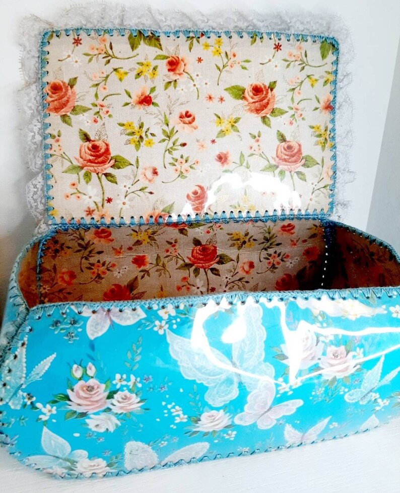 Pu&ograve; includere: Una scatola di immagazzinaggio floreale blu con un bordo di pizzo bianco e un coperchio con motivo floreale. La scatola &egrave; fatta di cartone e ha una finitura lucida.