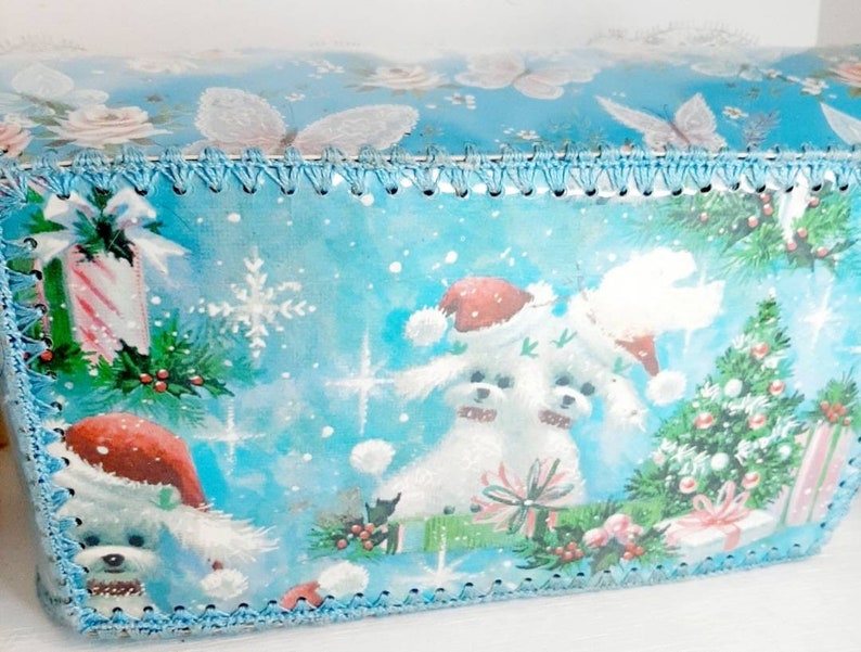 Pu&ograve; includere: Carta da regalo natalizia blu e bianca con un design di due cani bianchi con cappelli da Babbo Natale, un albero di Natale e bastoncini di zucchero. La carta ha un bordo di uncinetto blu attorno ai bordi.