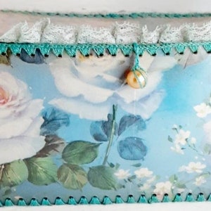 May include: A blue and white floral patterned box with a lace trim and a pearl button accent. The box is made of cardboard and has a scalloped edge.