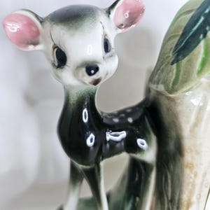 Könnte beinhalten: Keramik-Hirschfigur mit glänzendem Finish. Der Hirsch hat ein weißes Gesicht, rosa Ohren und einen dunkelgrünen Körper mit weißen Punkten. Die Figur ist ein dekorativer Gegenstand.
