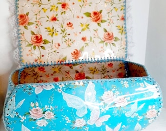 May include: A vintage blue and white floral storage box with a lace trim and a butterfly design. The lid is open and shows a floral pattern.