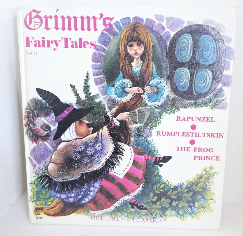 Puede incluir: Portada de libro vintage "Grimm's Fairy Tales". La ilustraci&oacute;n presenta a Rapunzel, una bruja y el texto "Rapunzel, Rumpelstiltskin, The Frog Prince". La portada tiene un fondo blanco con ilustraciones coloridas.