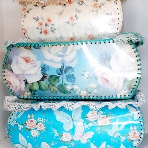 Pu&ograve; includere: Tre scatole di immagazzinaggio vintage con motivi floreali. La scatola superiore &egrave; bianca con rose rosa e un bordo di pizzo. La scatola centrale &egrave; blu con rose bianche e un bordo verde. La scatola inferiore &egrave; turchese con farfalle bianche e rose rosa.