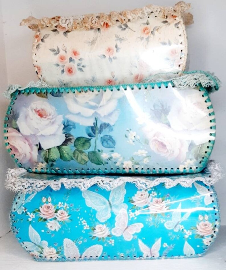 Pu&ograve; includere: Tre scatole di immagazzinaggio vintage con motivi floreali. La scatola superiore &egrave; bianca con rose rosa e un bordo di pizzo. La scatola centrale &egrave; blu con rose bianche e un bordo verde. La scatola inferiore &egrave; turchese con farfalle bianche e rose rosa.