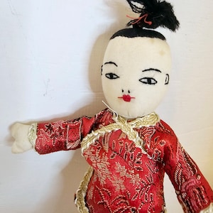 Puede incluir: Una muñeca de tela hecha a mano con cabello negro, un vestido bordado en rojo y dorado y una cara pintada.