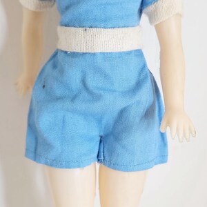 K&ouml;nnte beinhalten: Vintage Puppe in einem hellblauen Spielanzug mit wei&szlig;er Bord&uuml;re und wei&szlig;em G&uuml;rtel. Die Puppe hat einen roten Schal. Das blonde Haar der Puppe ist sichtbar. Ein Sammlerst&uuml;ck.