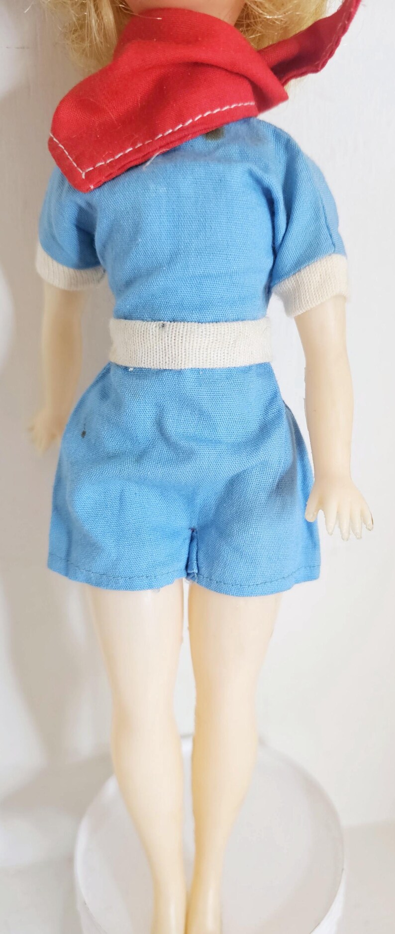K&ouml;nnte beinhalten: Vintage Puppe in einem hellblauen Spielanzug mit wei&szlig;er Bord&uuml;re und wei&szlig;em G&uuml;rtel. Die Puppe hat einen roten Schal. Das blonde Haar der Puppe ist sichtbar. Ein Sammlerst&uuml;ck.