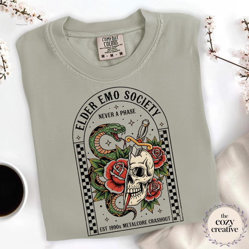 May include: Sage green sweatshirt with a graphic featuring a skull, snake, roses, and the text "ELDER EMO SOCIETY NEVER A PHASE". The design includes the text "EST 1990s METALCORE CRASHOUT". The sweatshirt has a crew neck and long sleeves.
