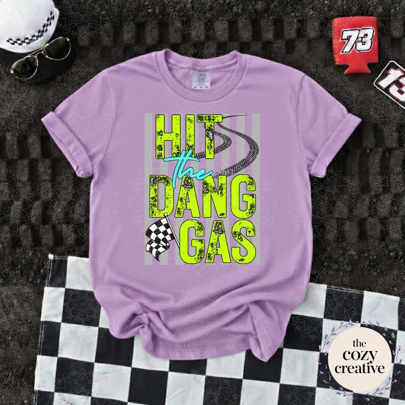May include: A lilac t-shirt featuring the neon green and teal text "HIT the DANG GAS", with tire tracks and a checkered flag design. The image also shows sunglasses, a hat, and a checkered flag.