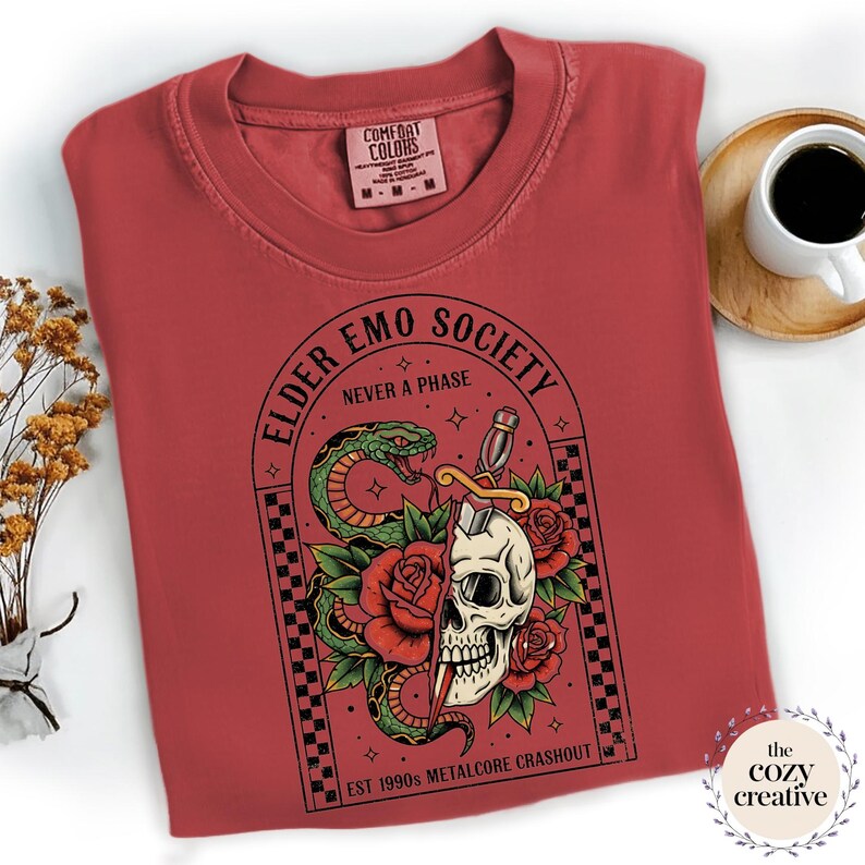 May include: A red Comfort Colors t-shirt with a graphic featuring a skull, snake, roses, and the text "ELDER EMO SOCIETY NEVER A PHASE". The design includes a sword and the text "EST 1990s METALCORE CRASHOUT".