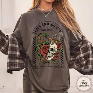 May include: Gray sweatshirt with a graphic featuring a skull bisected by a dagger, a green snake, and red roses. Text reads "ELDER EMO SOCIETY NEVER A PHASE" and "EST 1990S METALCORE CRASHOUT".