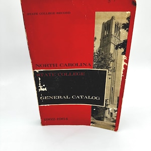 Puede incluir: Un catálogo vintage rojo y negro titulado "North Carolina State College General Catalog 1962-1964". La portada presenta una imagen en blanco y negro de un edificio alto. El catálogo está ligeramente desgastado.