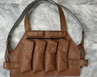 May include: Brown leather chest rig with multiple pouches and adjustable straps. Features four vertical pouches with snap closures, two smaller top pouches with zippers, and a wide shoulder strap. The rig is designed with a utilitarian aesthetic.
