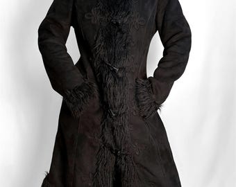 May include: A long black coat with faux fur trim on the collar, cuffs, and front. The coat has a suede-like texture and floral embroidery. It has a button closure and is knee-length. The coat is approximately 100 cm in length.
