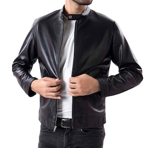 Könnte beinhalten: Schwarze Lederjacke mit Stehkragen und Reißverschluss vorne. Die Jacke hat lange Ärmel und eine taillierte Passform. Das Model trägt ein weißes T-Shirt darunter. Klassischer Stil.