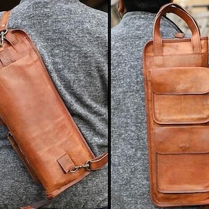 May include: A brown leather quiver with a shoulder strap and multiple pockets. The quiver is designed to be worn over the shoulder and has a rectangular shape with a flap closure. The leather has a natural, textured appearance.