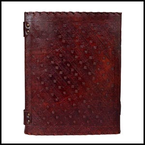 May include: A dark brown leather journal with an embossed pattern. The cover has a diagonal design of small squares and lines. The edges are stitched, and the journal features metal corner accents and a leather strap closure. The journal measures approximately 25 cm x 20 cm.