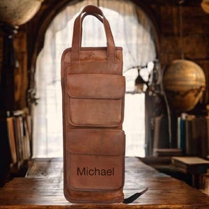 May include: A brown leather tote bag with two front pockets and a top handle. The word "Michael" is embossed on the lower pocket. The bag is made of a rich, textured leather.
