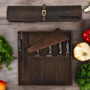 Puede incluir: Un estuche para cuchillos de cuero marrón con cierre de hebilla, desenrollado para revelar varios cuchillos. El texto "TEXT HERE" es visible en el rollo cerrado. Los cuchillos están en un estuche de cuero marrón.