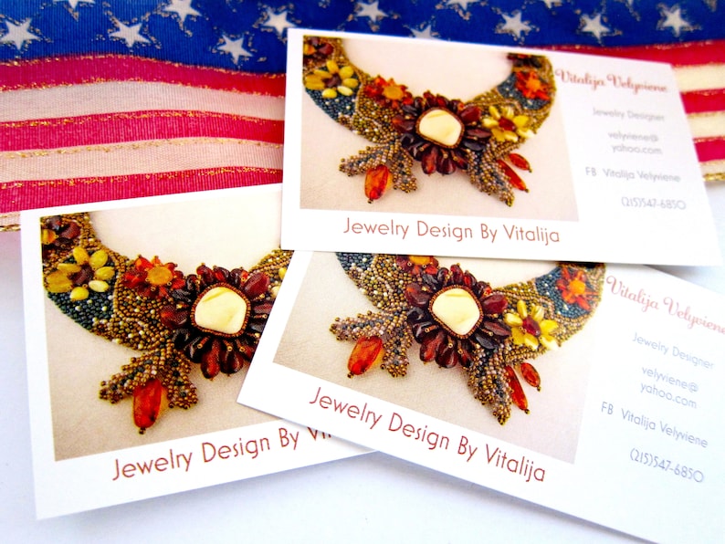 May include: Three business cards with a photo of a beaded necklace with a large amber-colored stone in the center. The text on the cards reads "Jewelry Design By Vitalija" and includes contact information for the designer.