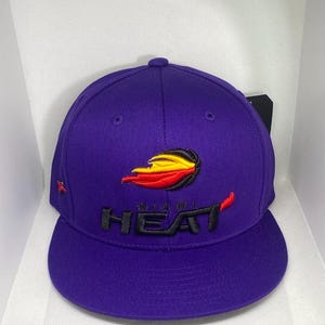 May include: A purple baseball cap featuring the Miami Heat logo. The logo is a stylized flame in red, yellow, and black, with the word "HEAT" in black. A small red "R" is embroidered on the side of the cap.