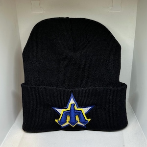 Peut inclure: Bonnet en tricot noir avec un bord replié. Le bonnet présente un écusson en forme d'étoile avec un logo bleu et jaune. Le chapeau est fait d'un matériau doux et tricoté.