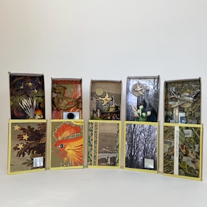 May include: A collection of ten small, rectangular boxes with various decorative elements. The boxes feature images of a rooster, a castle, a plane, and other designs. The boxes are arranged in two rows, with a yellow border.