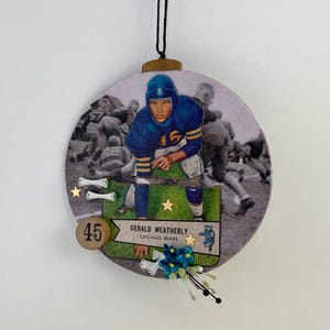 May include: A round, wooden ornament with a vintage football player image. The player is wearing a blue jersey with the number 15. The ornament has a gold number 45, a gold star, and a white bone. The text on the ornament reads "Gerald Weatherly, Chicago Bears".