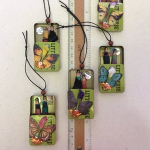 May include: Five small, green, rectangular boxes with a hinged lid. Each box features a different butterfly design and the text "Little Fuse" on the front. The boxes are hanging from black cords.