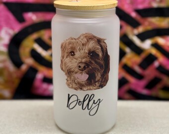 May include: A frosted glass tumbler with a bamboo lid and a clear straw. The tumbler features a brown and tan dog portrait and the name "Dolly" in a script font. The background is a colourful abstract design.
