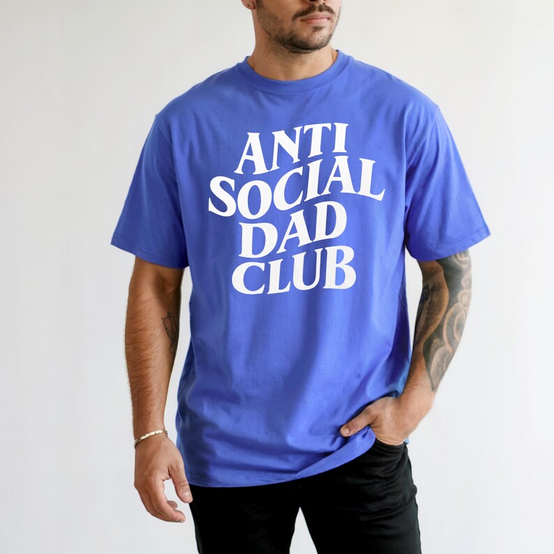 Puede incluir: Una camiseta azul con el texto blanco "ANTI SOCIAL DAD CLUB". La camiseta tiene mangas cortas y cuello redondo. La persona lleva pantalones negros.