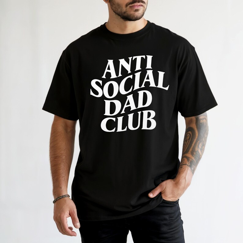 Puede incluir: Camiseta negra con el texto blanco "ANTI SOCIAL DAD CLUB" en una fuente en negrita sin serifa. La camiseta es de estilo cuello redondo cl&aacute;sico, y el texto est&aacute; centrado en el pecho.