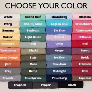 Puede incluir: Una exhibici&oacute;n de camisetas dobladas en varios colores, incluyendo blanco, azul, rosa y negro. El texto "CHOOSE YOUR COLOR" est&aacute; en la parte superior, con nombres de colores como "Blossom", "Chili" y "True Navy" etiquetando cada pila. Las camisetas est&aacute;n bien ordenadas.