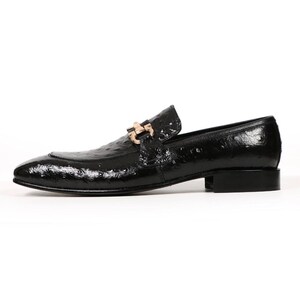 May include: A black leather loafer with a textured finish and a gold-colored buckle. The shoe has a low heel and a pointed toe. The loafer is a classic style of footwear.
