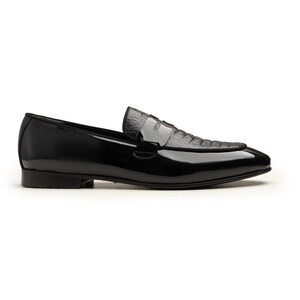 May include: A black leather loafer with a glossy finish. The shoe features a textured vamp and a sleek, pointed toe. The design includes a low heel and a slip-on style, suitable for formal or semi-formal occasions.