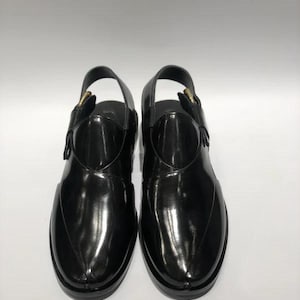 May include: Pair of black leather sandals with a glossy finish. The sandals have a slingback design with a buckle closure and a rounded toe. The soles are black and the sandals appear to be unworn.