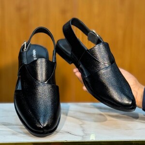 Op de afbeelding: Twee zwarte leren sandalen met een getextureerde afwerking. De sandalen hebben een slingback-band met een gesp en een gesloten teenontwerp. De schoenen worden gepresenteerd op een marmeren oppervlak.