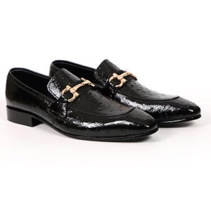 May include: A pair of black patent leather loafers with a gold-colored buckle detail. The shoes have a glossy finish and a low heel, suitable for formal or semi-formal occasions.