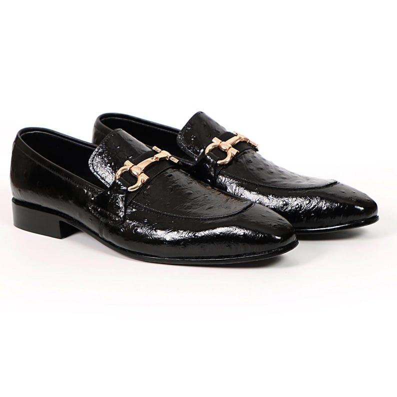 May include: A pair of black patent leather loafers with a gold-colored buckle detail. The shoes have a glossy finish and a low heel, suitable for formal or semi-formal occasions.