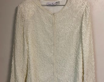 May include: Ivory-colored jacket with intricate beaded detailing. The long-sleeved garment features a delicate, swirling pattern of small beads, a round neckline, and a full-length zipper. The label reads "Laurence Kazar".