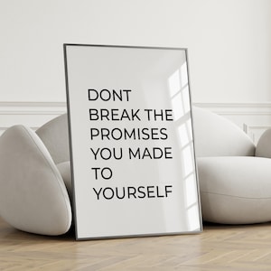 May include: A framed print with the text "DON'T BREAK THE PROMISES YOU MADE TO YOURSELF" in black against a white background. The frame is black and the print is leaning against a white sofa.
