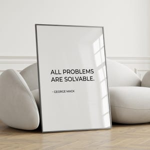 May include: A framed print with the text "ALL PROBLEMS ARE SOLVABLE." and the author's name, George Mack. The print has a white background and a black frame. The print is leaning against a white chair.