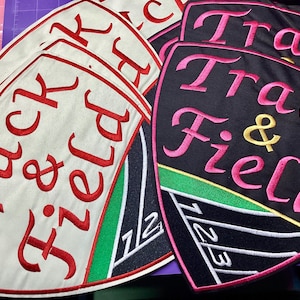 May include: Embroidered patches with the words "Track & Field" in red and pink script. The patches are shield-shaped with a white or black background, and a track and field design.