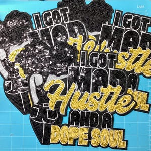 May include: A collection of embroidered patches featuring a figure with a large afro hairstyle and the text I GOT MAD HUSTLE AND A DOPE SOUL. The patches are decorated with black and yellow sequins, showcasing a detailed design of a person.